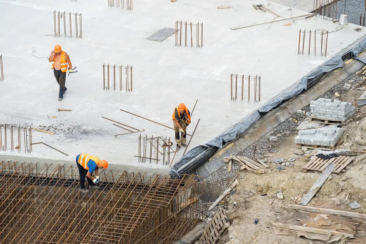 Workers on a concrete deck between rebar cages on a commercial jobsite, seen from above