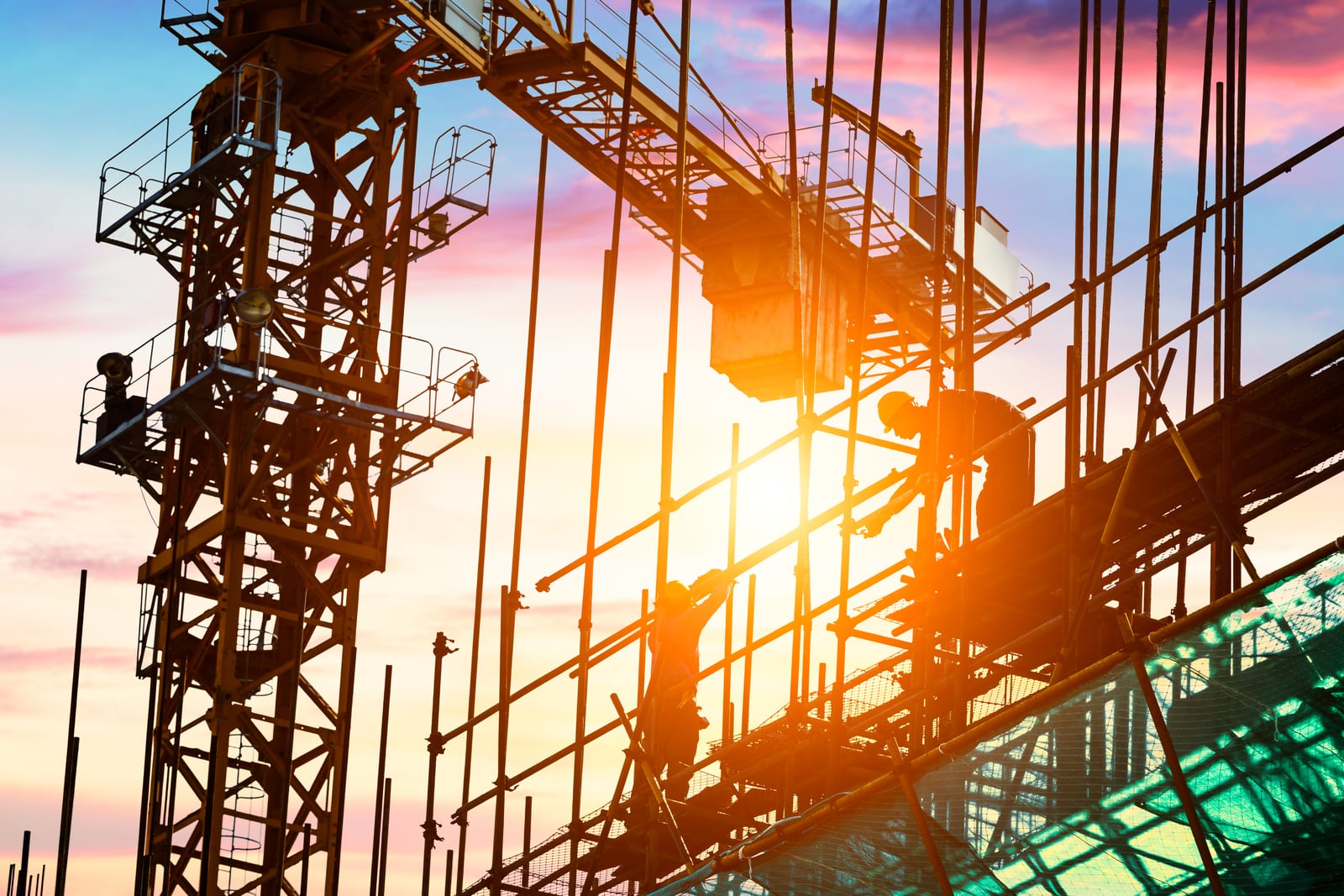 Silhouetted construction workers on scaffolding beside a tower crane at sunset, the kind of jobsite where AI notetakers and pocket recorders on a superintendent's phone quietly become company business records.